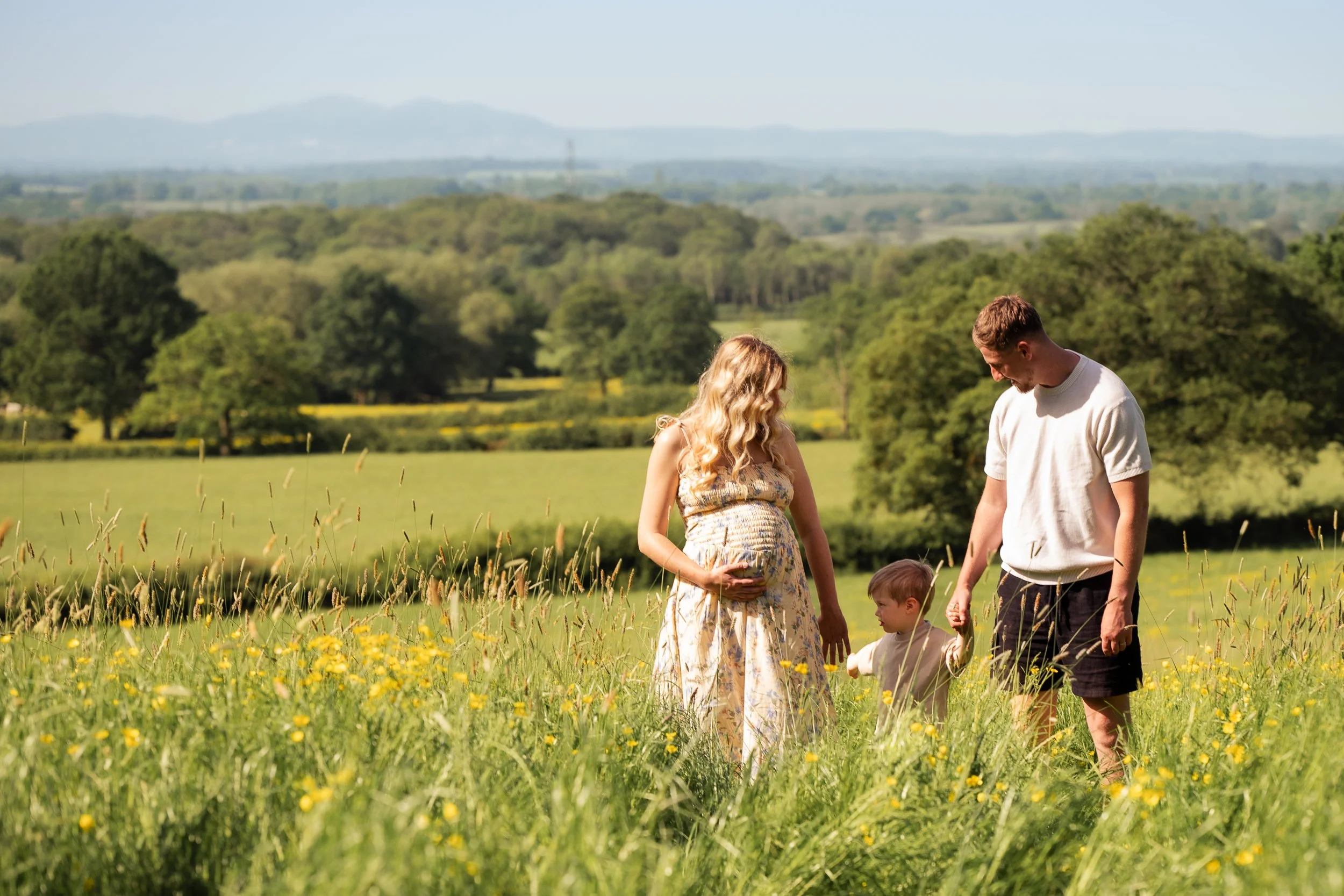 Family walking in buttercup field in Worcestershire during a maternity photoshoot with Chloe bower photography