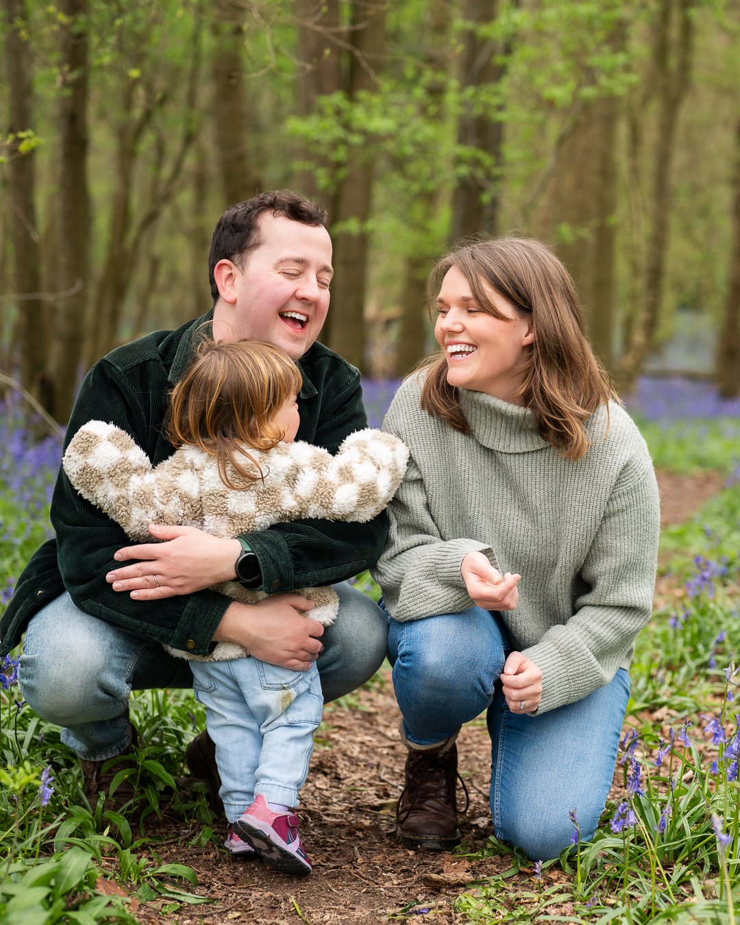 Mum and dad hugging toddler in the bluebells during a family photoshoot