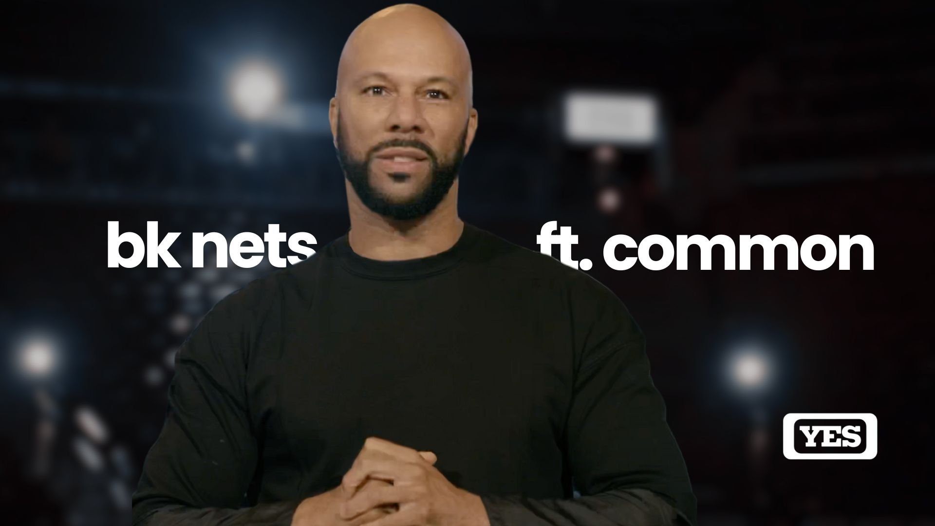A man with a shaved head and beard wearing a black shirt, standing in front of a dark background with blurred lights, with text overlaid that reads 'bk nets ft. common', and a YES logo in the bottom right corner.