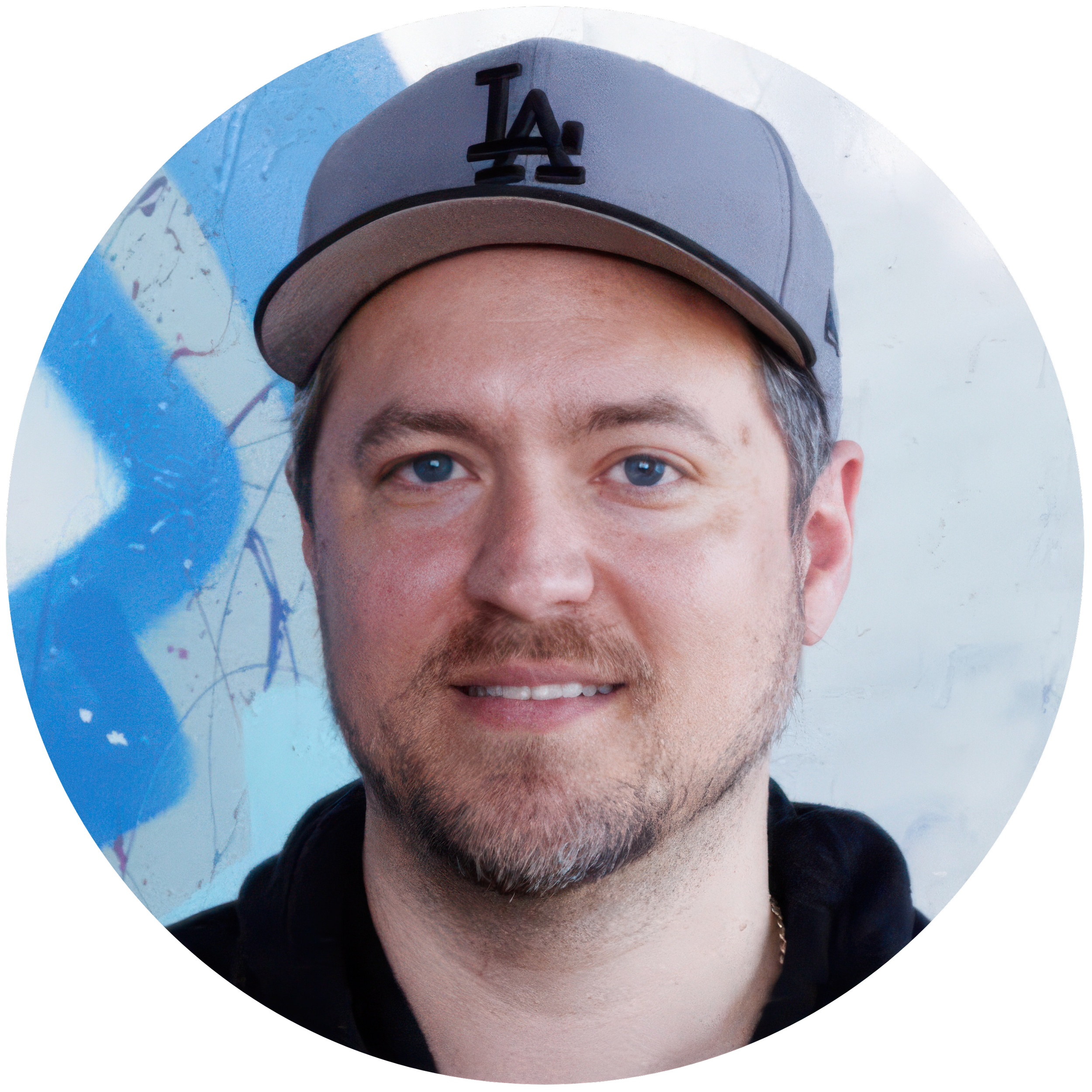 Close-up of a person's face wearing a gray baseball cap, with blue eyes and facial hair, against a graffiti background.
