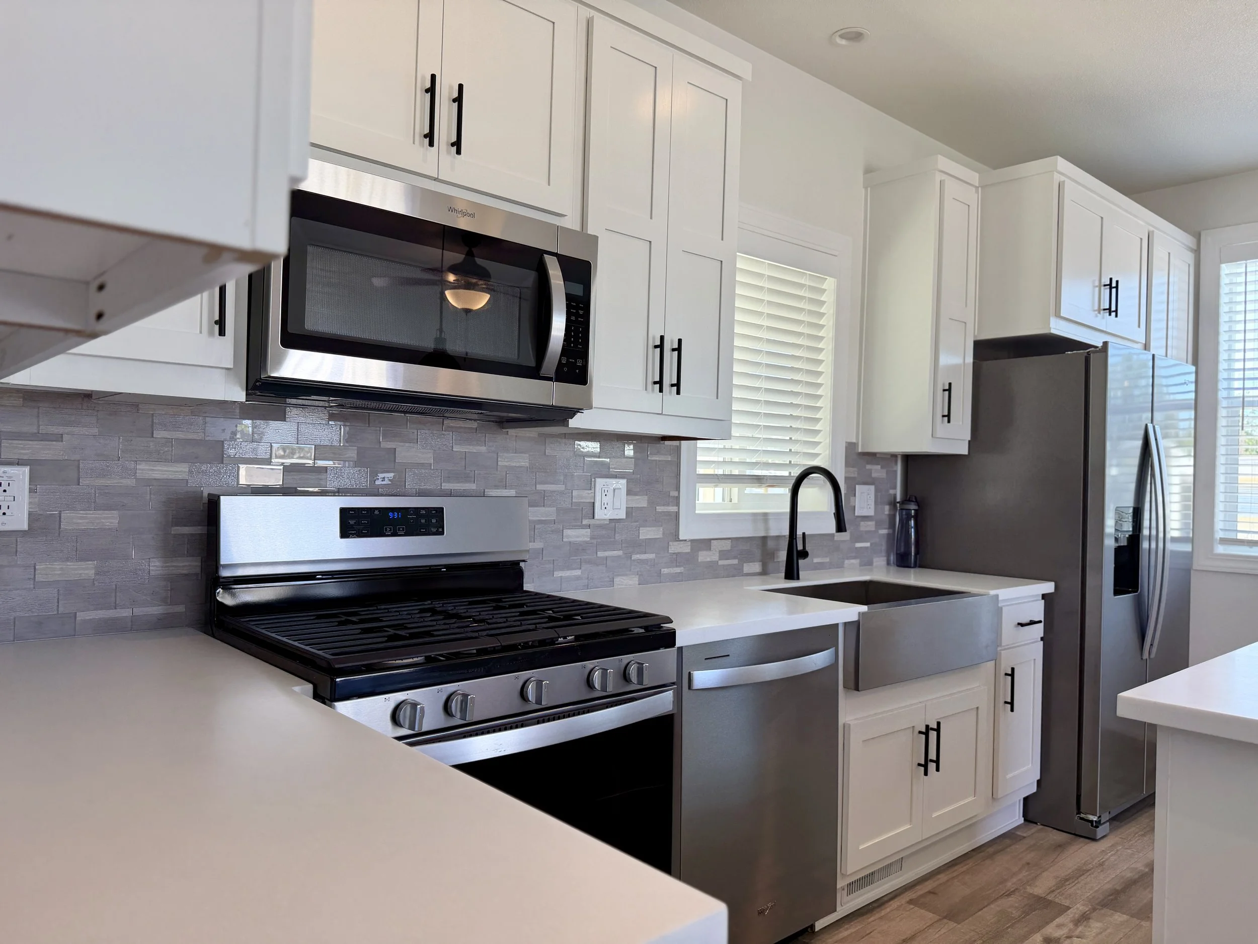 Modern kitchen with white cabinets, stainless steel microwave and stove, gray tile backsplash, and a black faucet over a white countertop.