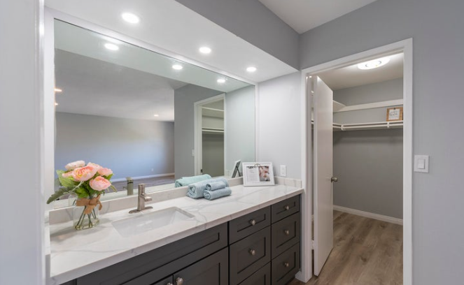 Bathroom vanity with a large mirror, flowers, rolled towels, and a view into a walk-in closet.