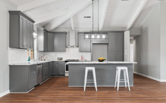 Modern kitchen with gray cabinets, white countertops, center island with two white stools, and hardwood floors.