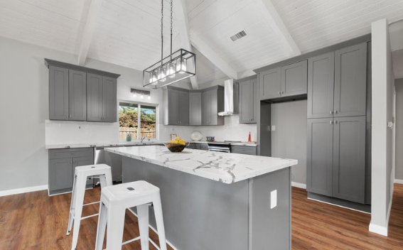 Modern kitchen with gray cabinets, white marble island, wooden floor, and a pendant light fixture.