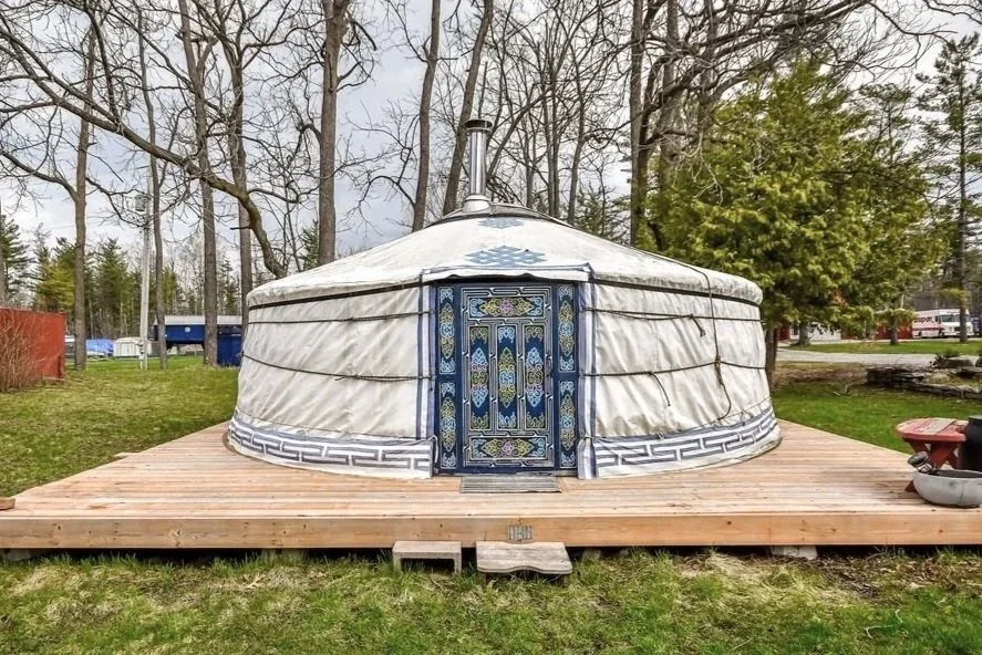 A yurt with a patterned door on a wooden deck in an outdoor setting surrounded by trees and grassy area.