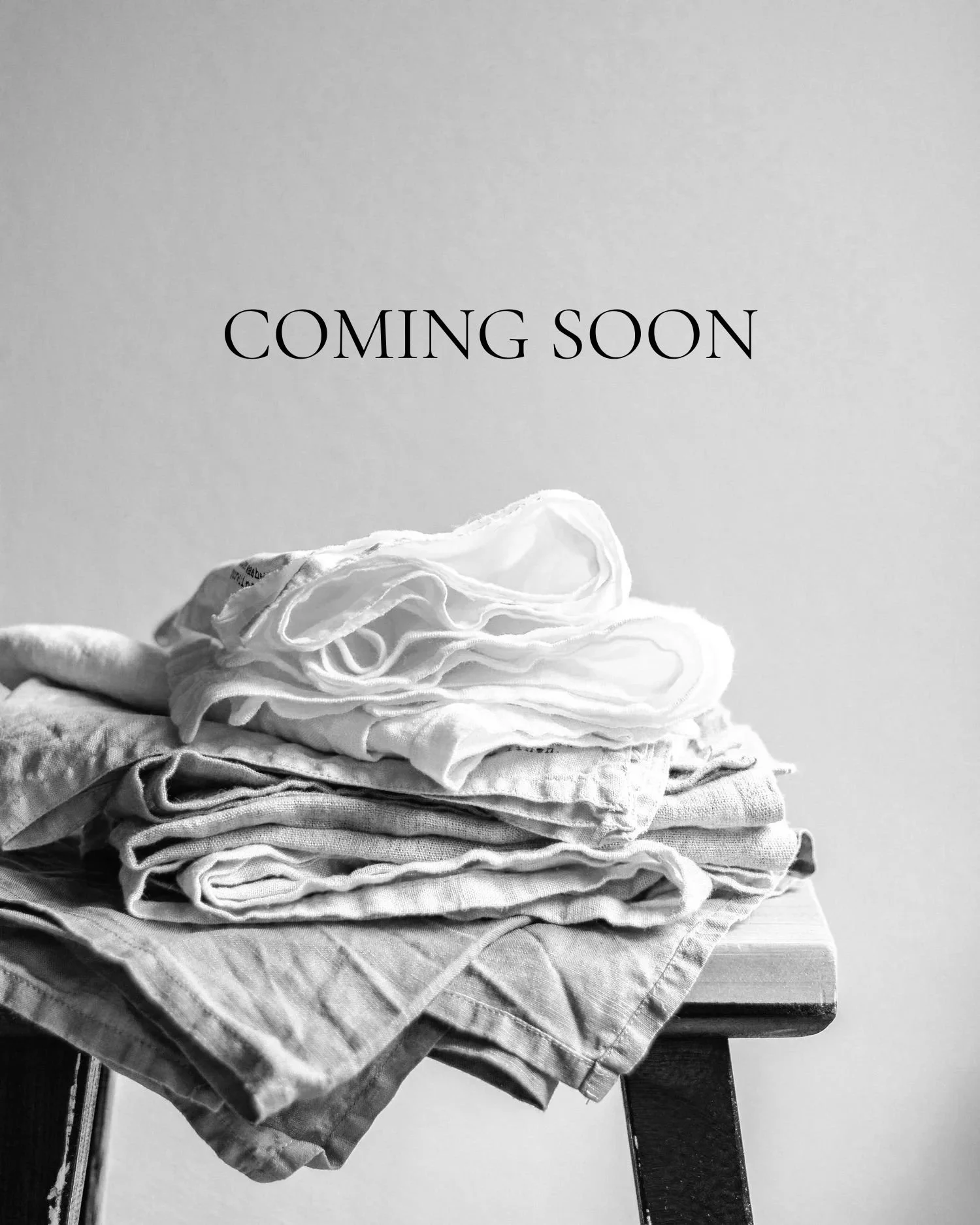 A pile of folded clothes on a table with a 'Coming Soon' sign hanging above.