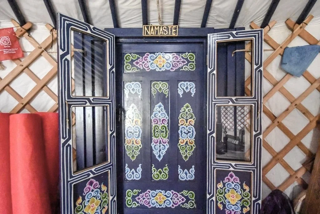 Decorative black wardrobe with colorful floral and swirl patterns and a 'Namaste' sign on top, situated in a yurt.