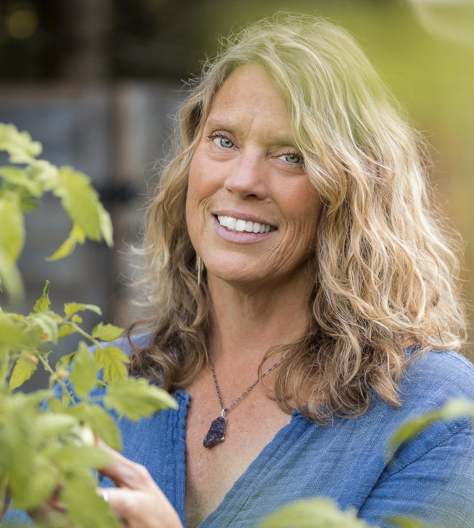 Kathy Bero smiling outdoors with greenery in the foreground and background.