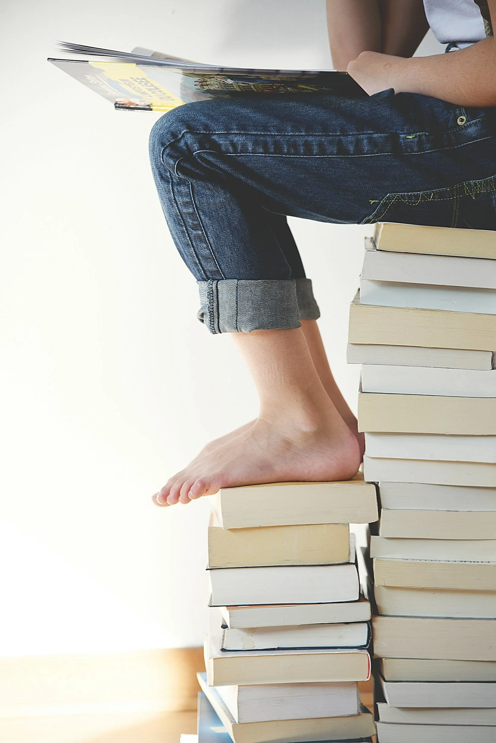 Person sitting with feet on books stacked on a white desk, reading a magazine, with a white background.