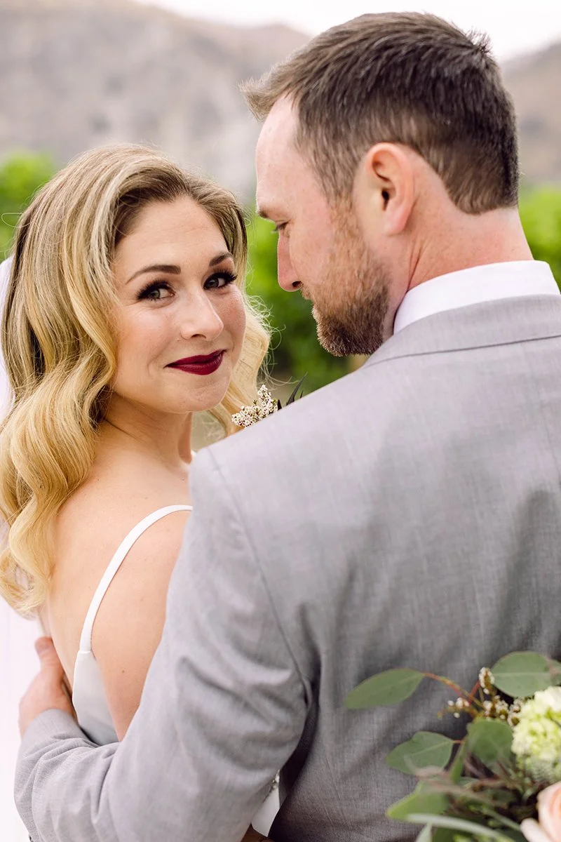 A bride and groom sharing a close moment, outdoors with a mountain background.