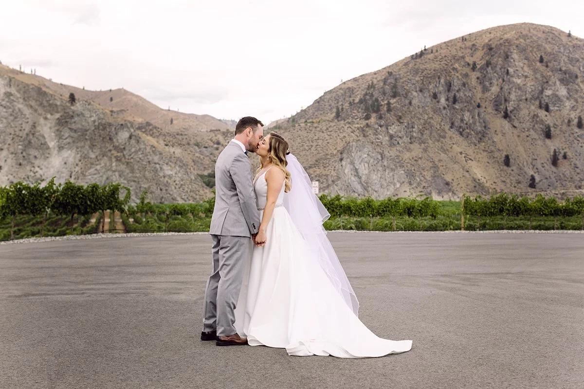 Bride and groom on wedding day sharing a kiss in an outdoor setting with mountainous background.