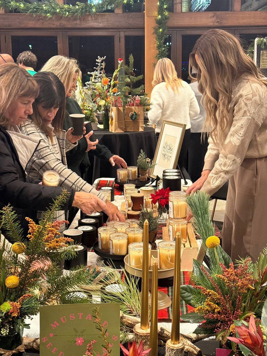 People shopping for candles and holiday decorations at a festive event, with Christmas flowers, candles, and greenery on display.