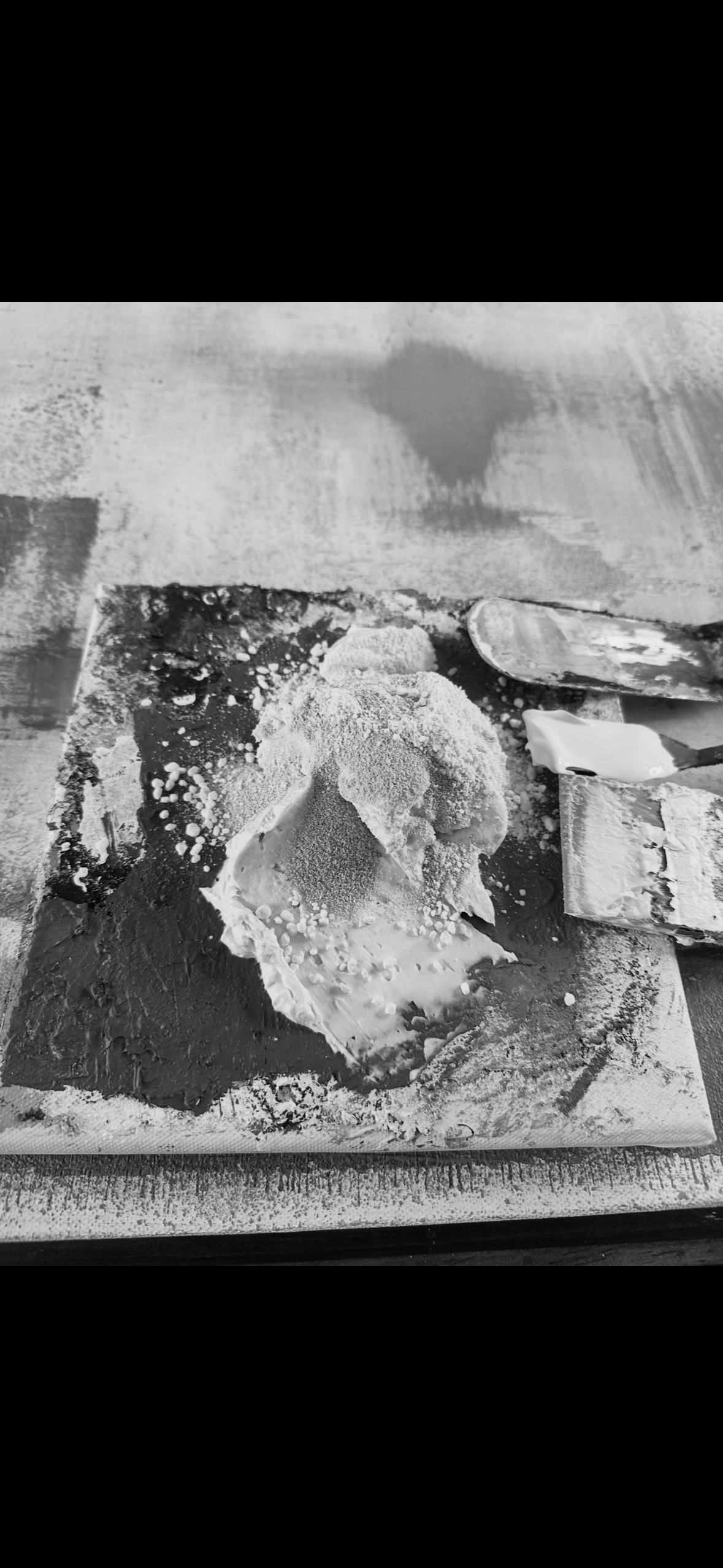 A large lump of ice cream or dough covered with powdered sugar, sitting on a spatula and surrounded by baking tools, on a wooden surface.