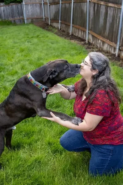 Fifi Heurlin, certified Ortho-Bionomy® practitioner, connecting nose to nose with a large black dog outdoors, offering gentle animal bodywork sessions in Vancouver, WA