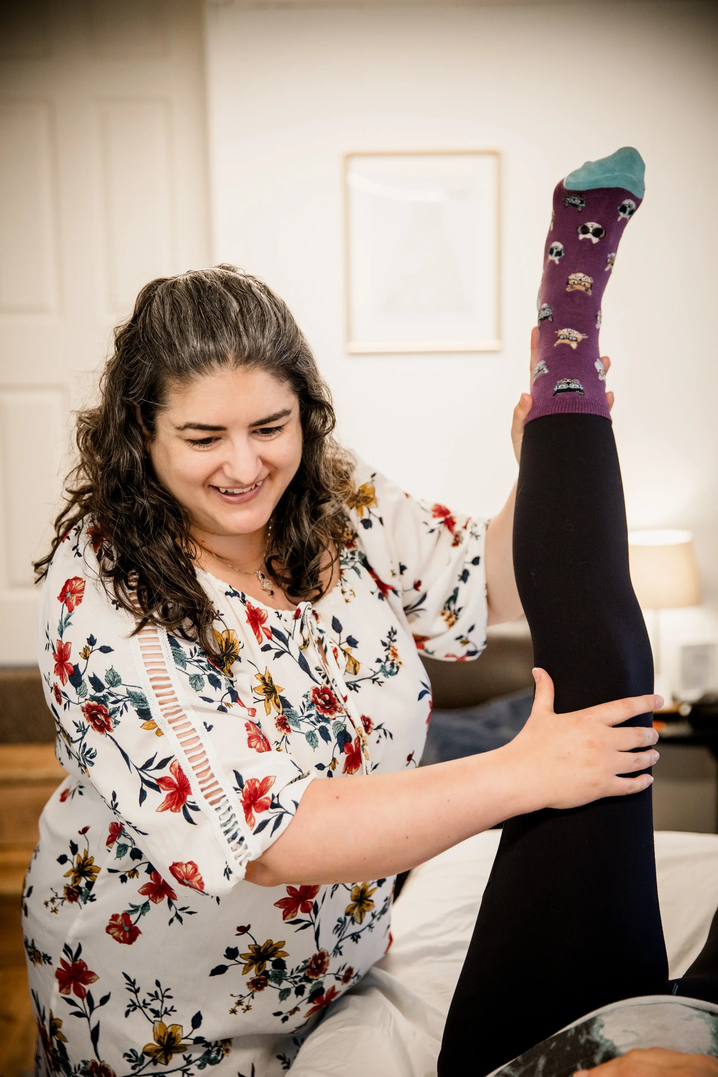 Fifi Heurlin, certified Ortho-Bionomy® practitioner, smiling while gently lifting and supporting a fully clothed client's leg during a bodywork session in Vancouver, WA