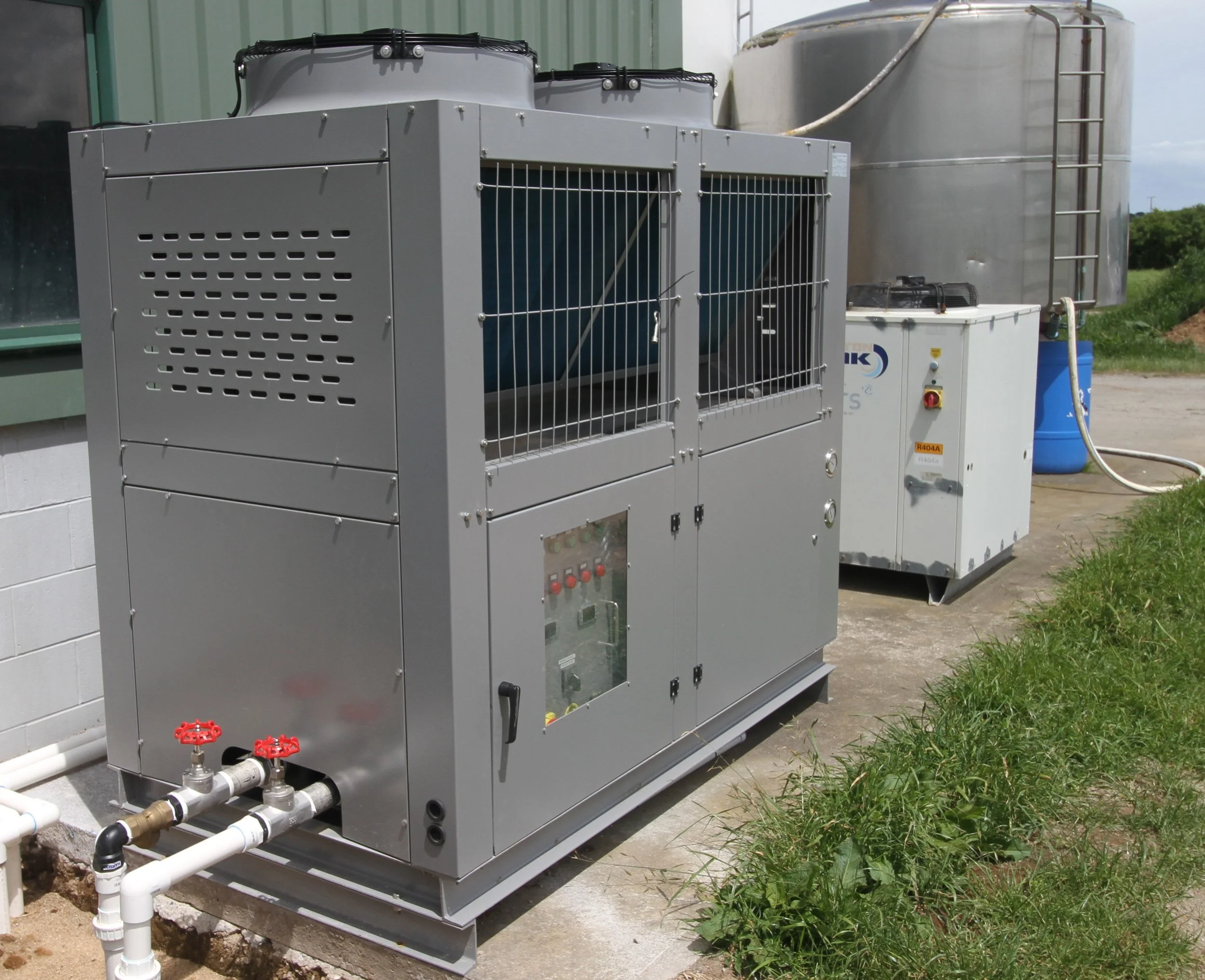 Outdoor industrial HVAC or refrigeration unit with pipes and control panel outside a building.