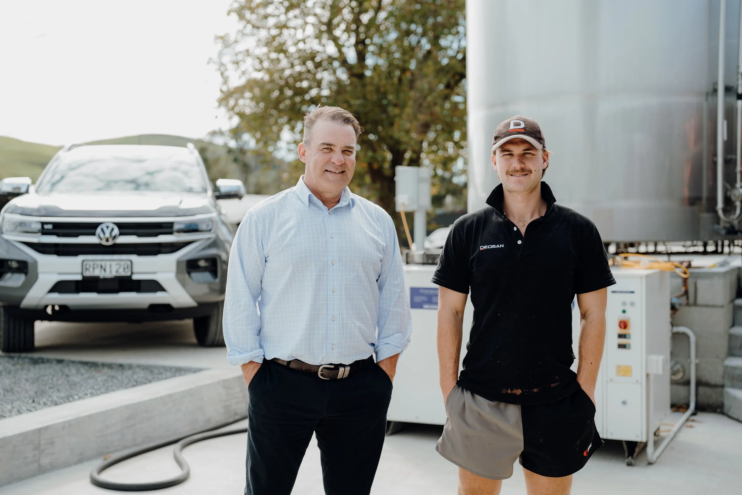 Owner Kip and son Seb standing outdoors, with a Terravest branded vehicle and machinery behind them. One is dressed in a light blue shirt, and the other in a black shirt and cap.