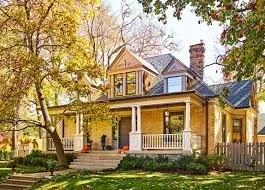 A large, Victorian-style house with a porch, surrounded by trees and lawn, during daytime.