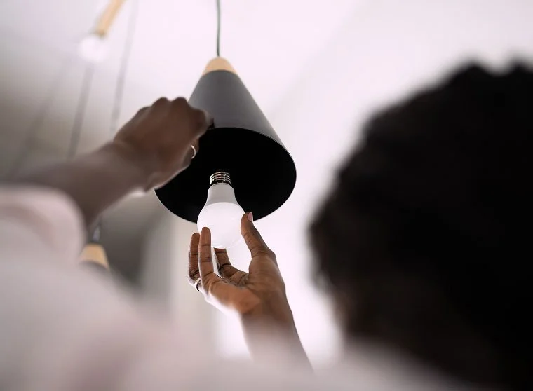 Person installing a light bulb into a ceiling fixture in a room with hanging pendant lights.