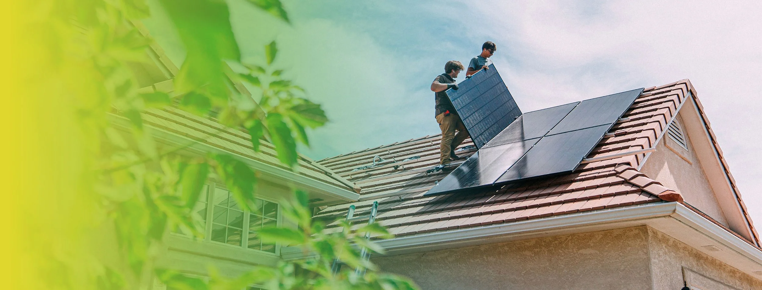 Two workers installing or maintaining solar panels on a residential house roof under a blue sky.