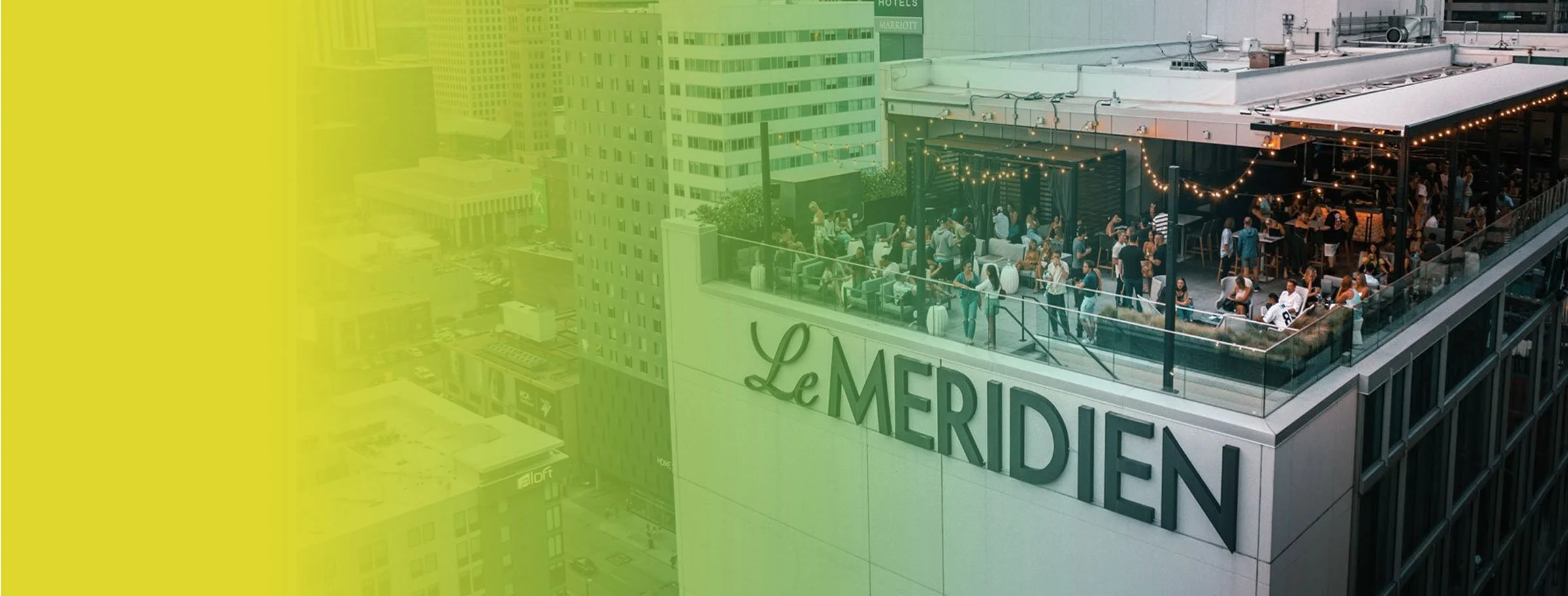 Cityscape rooftop with people socializing on outdoor terrace overlooking buildings, with 'Le Meridien' sign on the building.