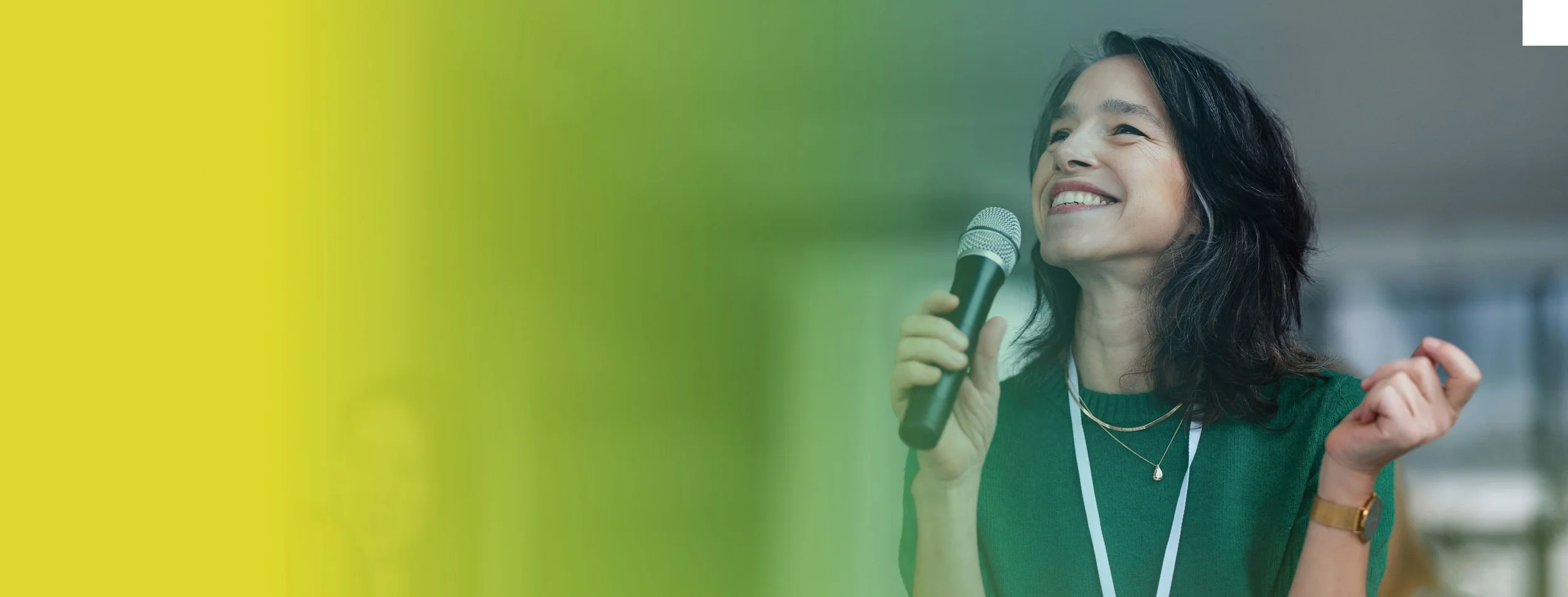 A woman holding a microphone and smiling, standing in a conference or event space.