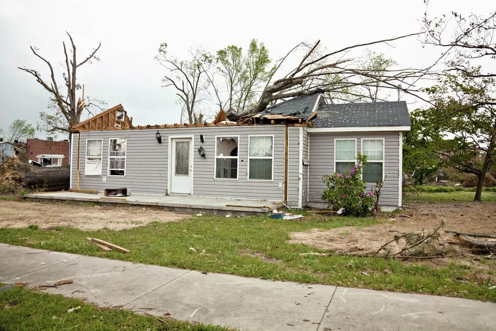 A house with a damaged roof and fallen tree, indicating storm or tornado destruction.