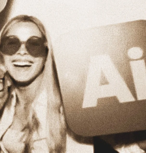 A smiling woman with sunglasses and long hair standing next to a sign with the letter 'A' on it.