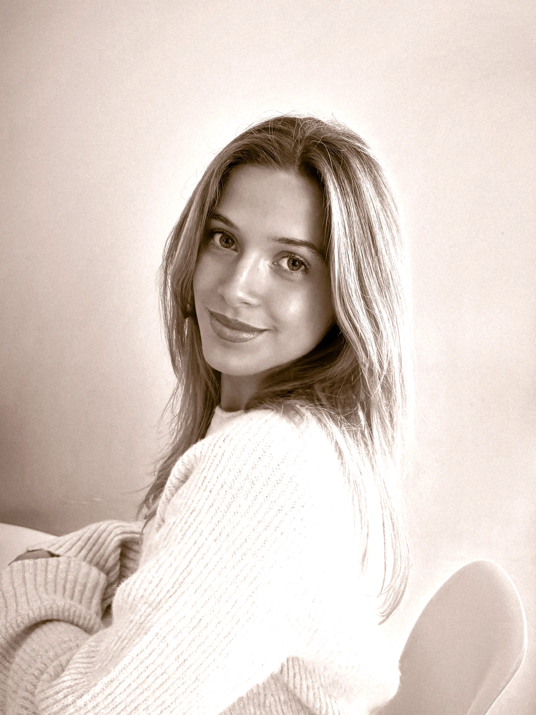 A young woman with long, wavy hair smiling at the camera, wearing a cozy, knitted sweater.