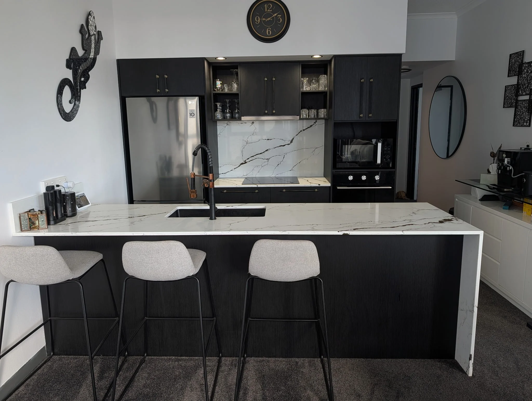 Modern kitchen with black cabinetry, quarts stone backsplash, and a large island with beige chairs.