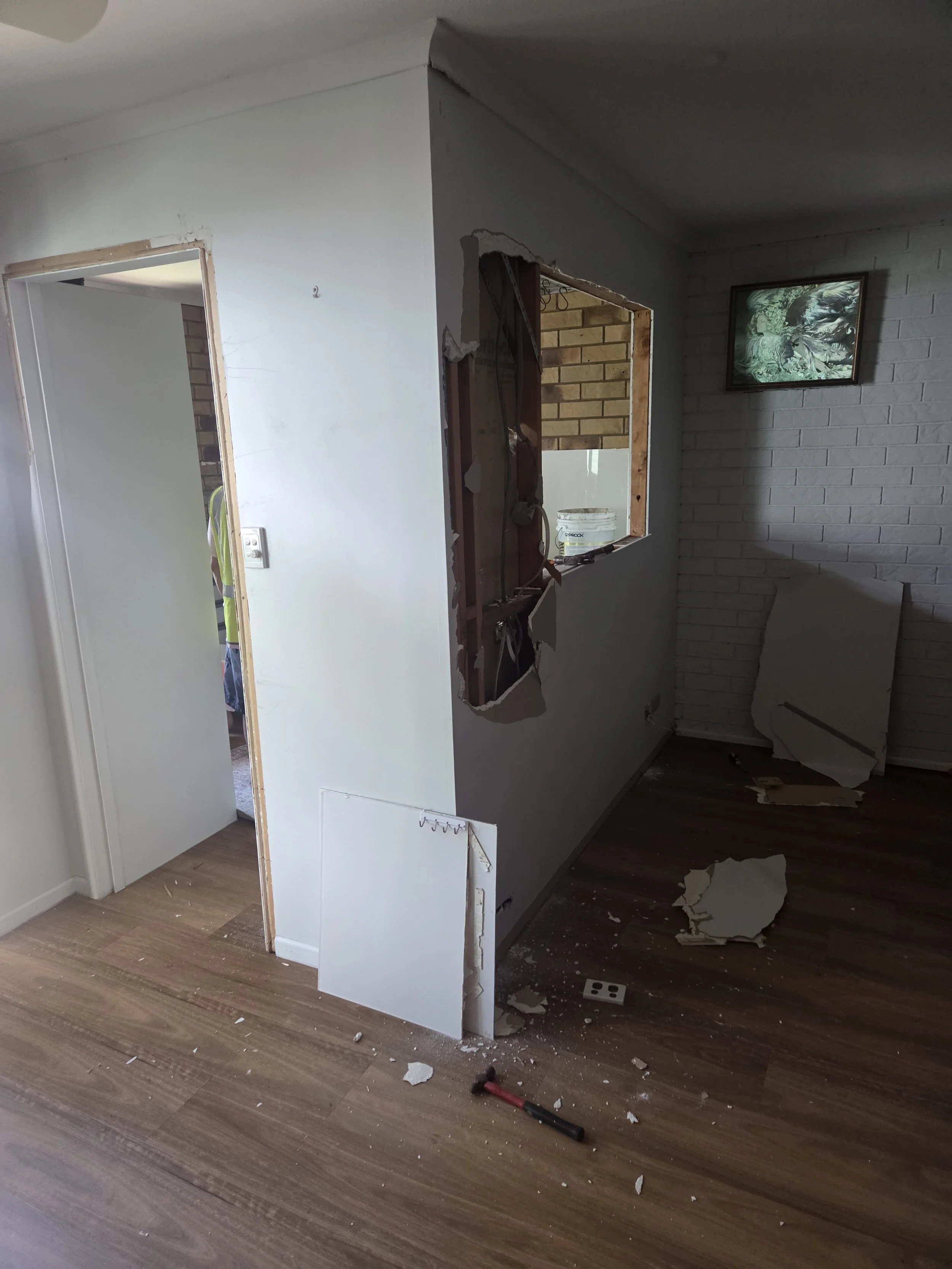 Interior room with  two walls to be removed, exposing the wooden studs and plumbing behind.