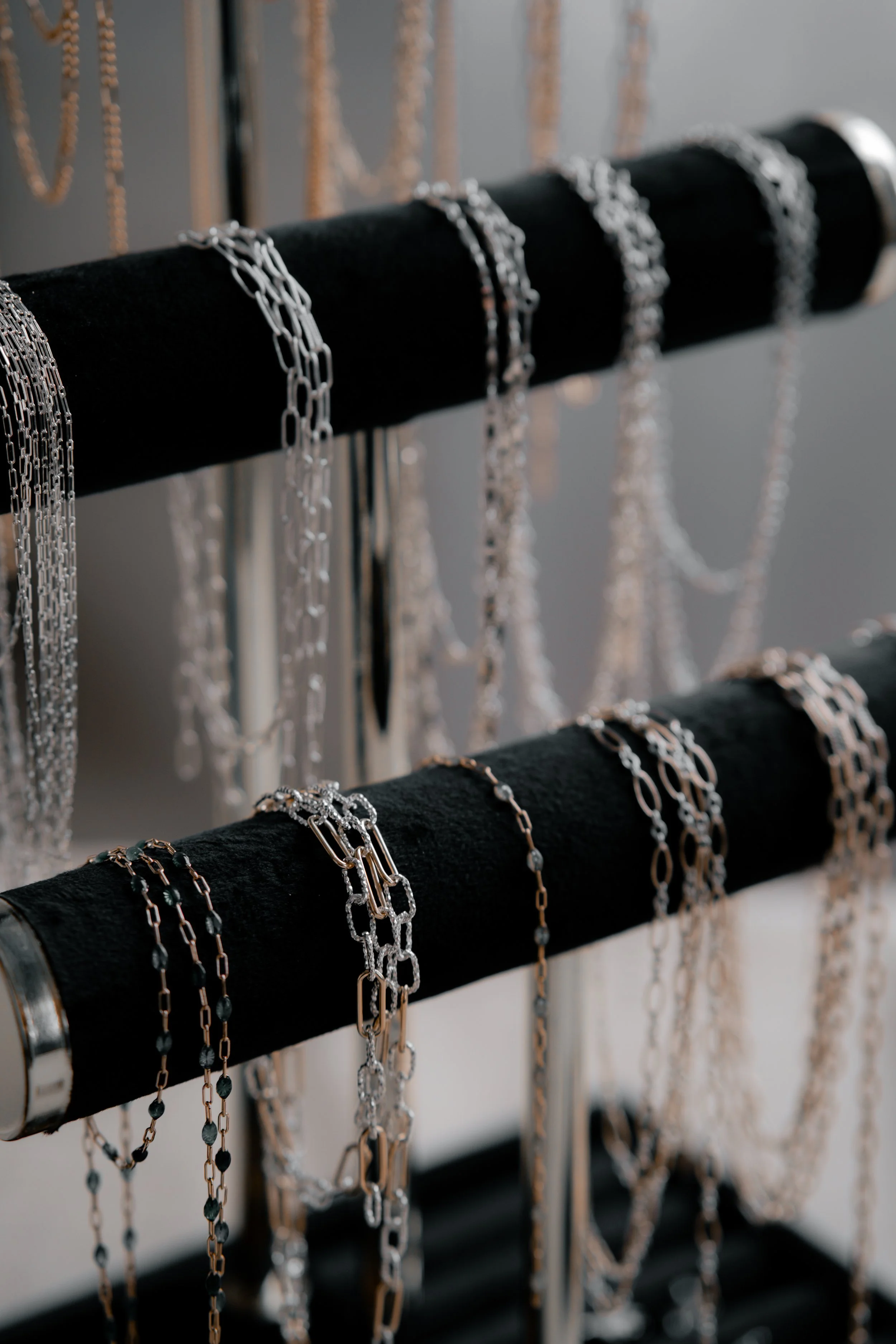 Multiple silver and gold necklaces hanging on black velvet display rods in a jewelry store.