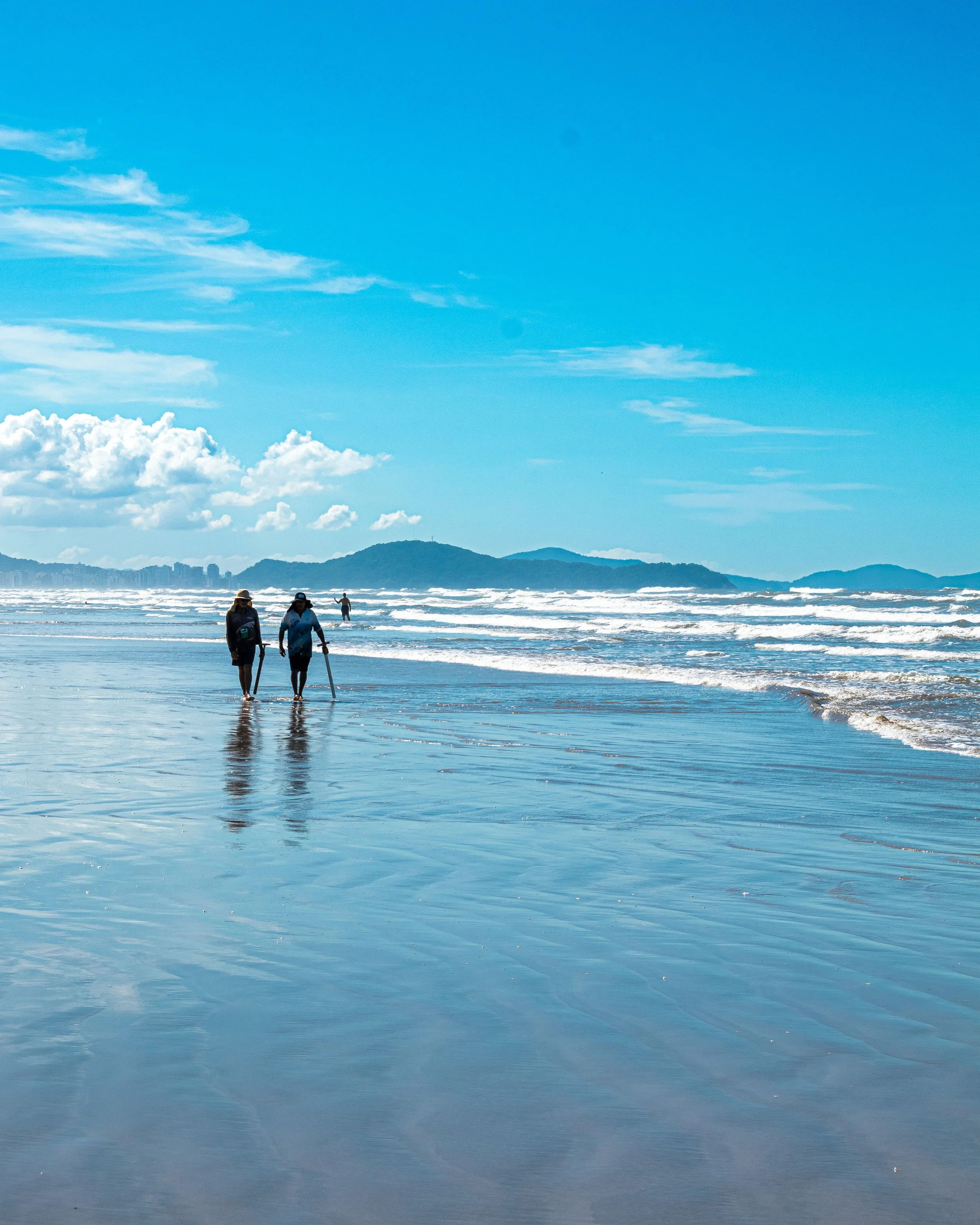 Two people walking along a beach shoreline with mountains in the background, representing mindfulness and connection