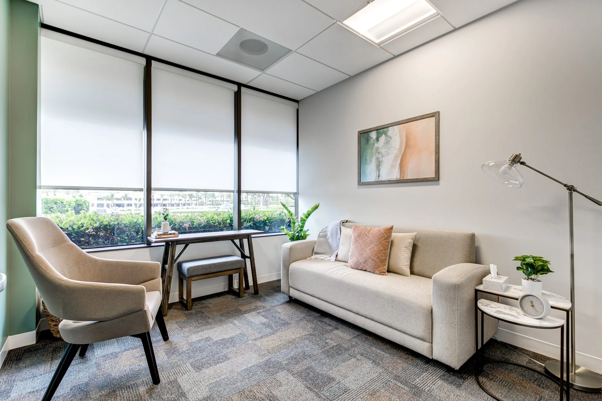 Calming therapy office waiting room at Coastline Psychology with beige armchair, sofa, and large windows overlooking greenery