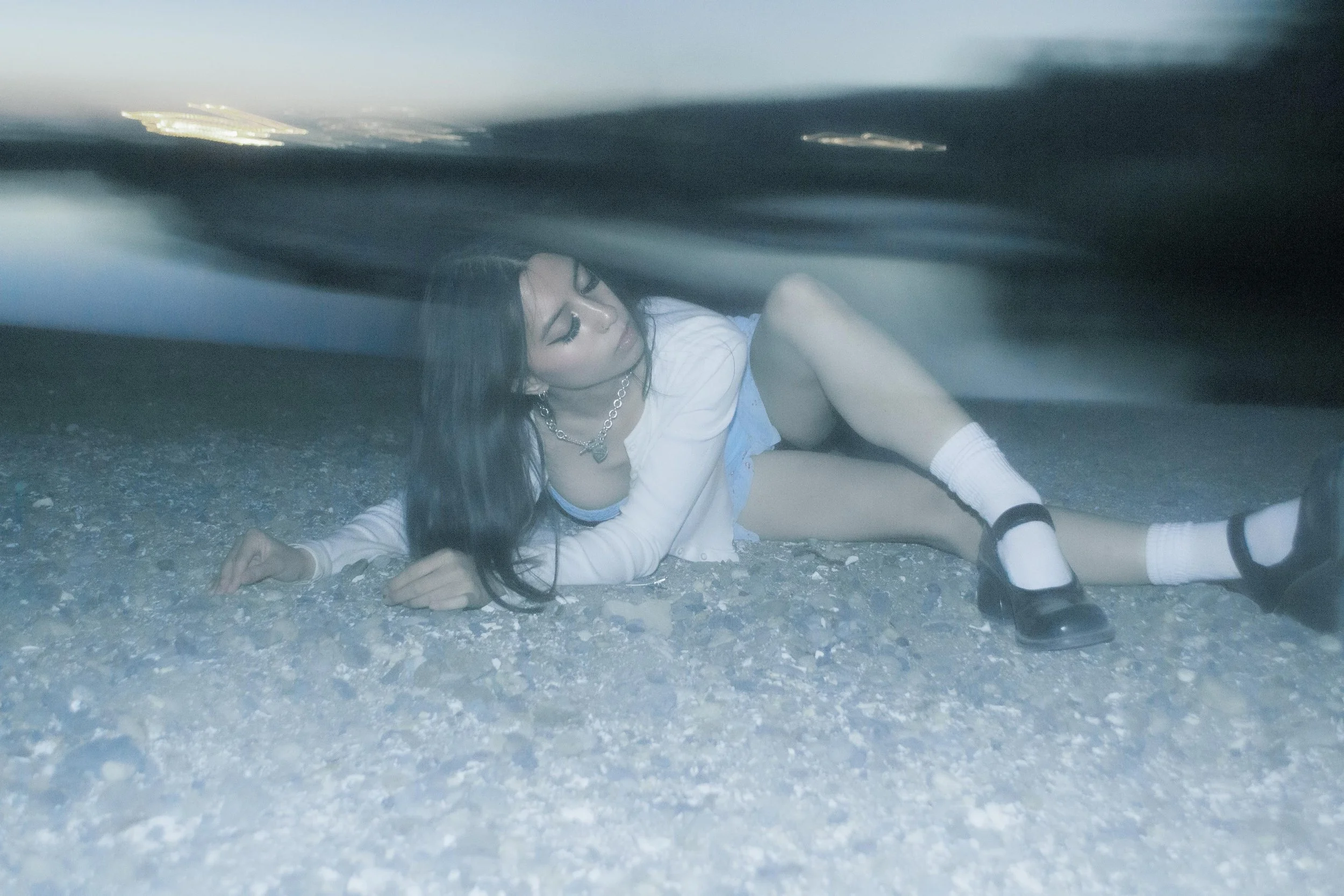 A woman lying on the ground under a car, looking up with a worried expression.