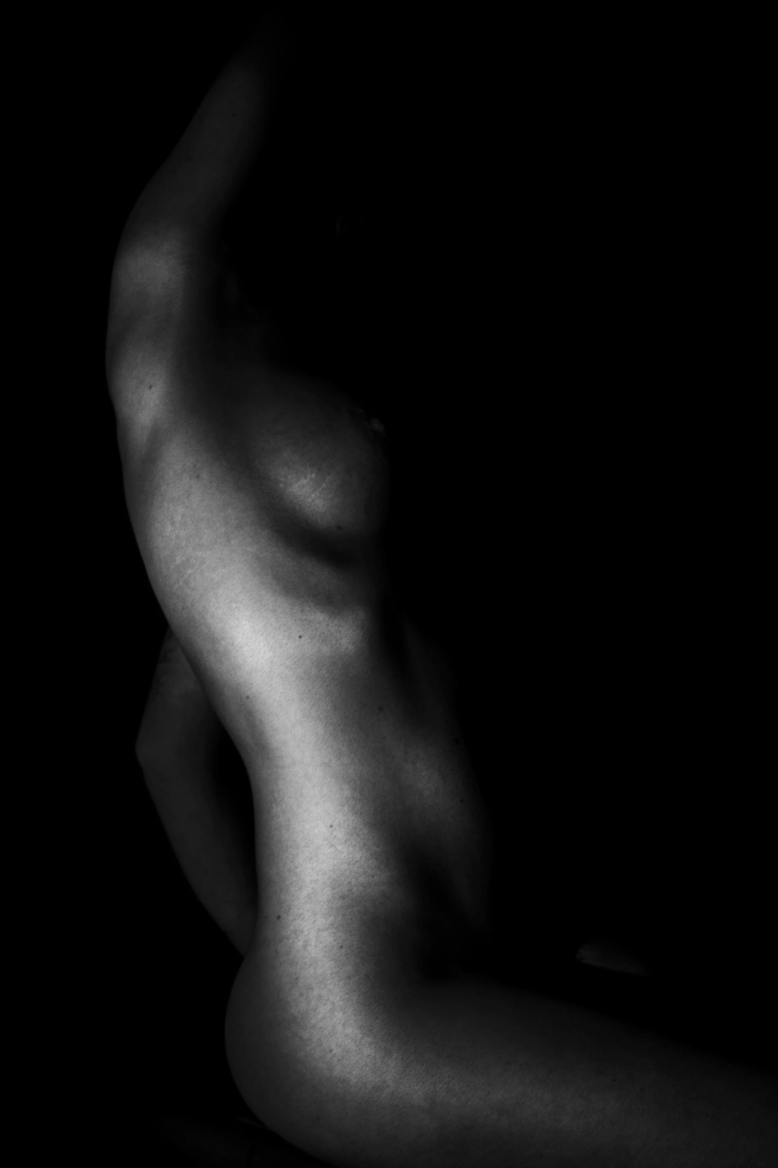 Black and white photo of a person's back, shoulder, arm, and part of the neck with dramatic lighting emphasizing the contours of the body.