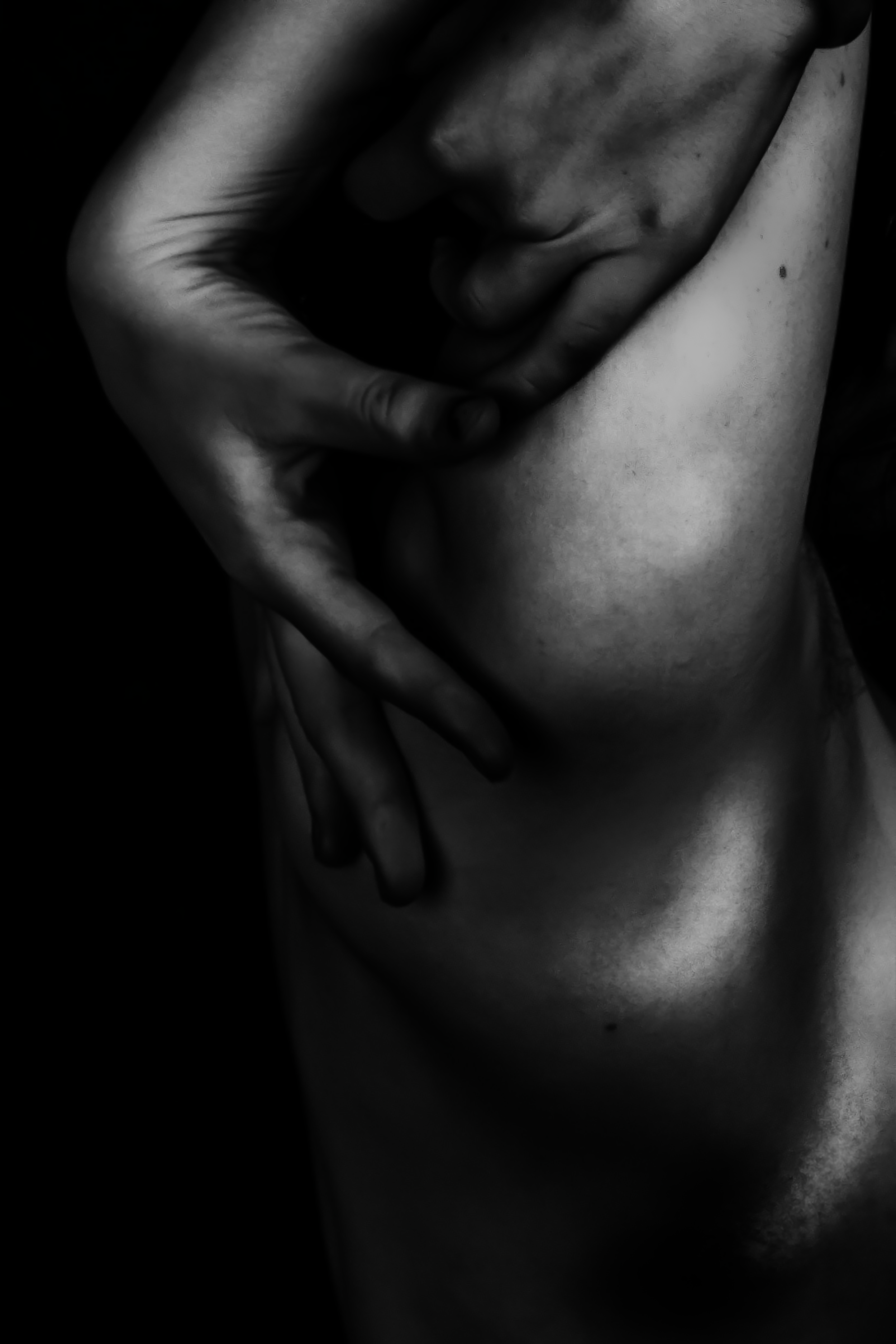 A black and white close-up photograph of two hands, with one hand gently touching the face of a person with closed eyes, conveying a sense of intimacy and tenderness.