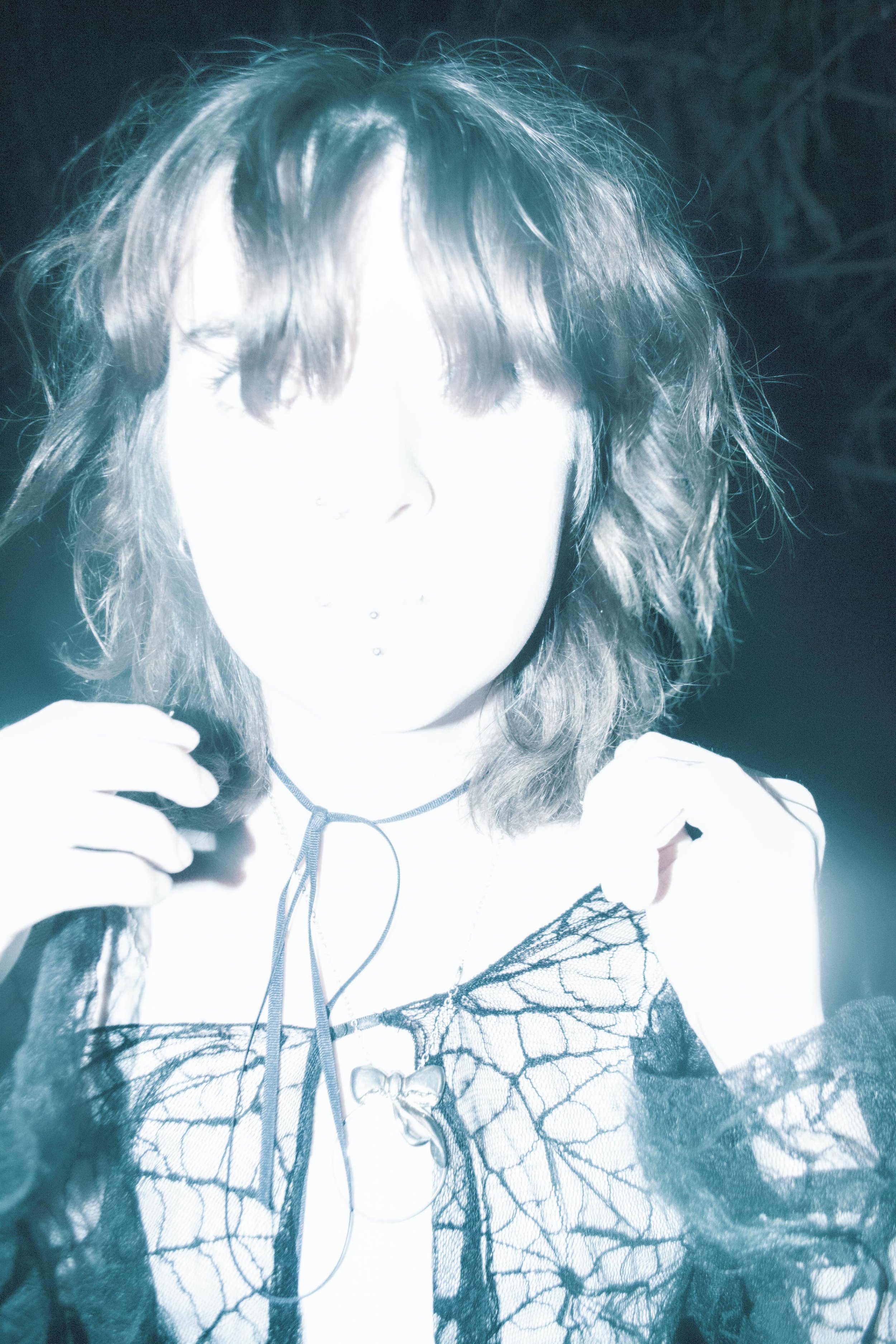 A person with curly hair is holding headphones, with a bright, overexposed face and a background featuring trees and dark sky.