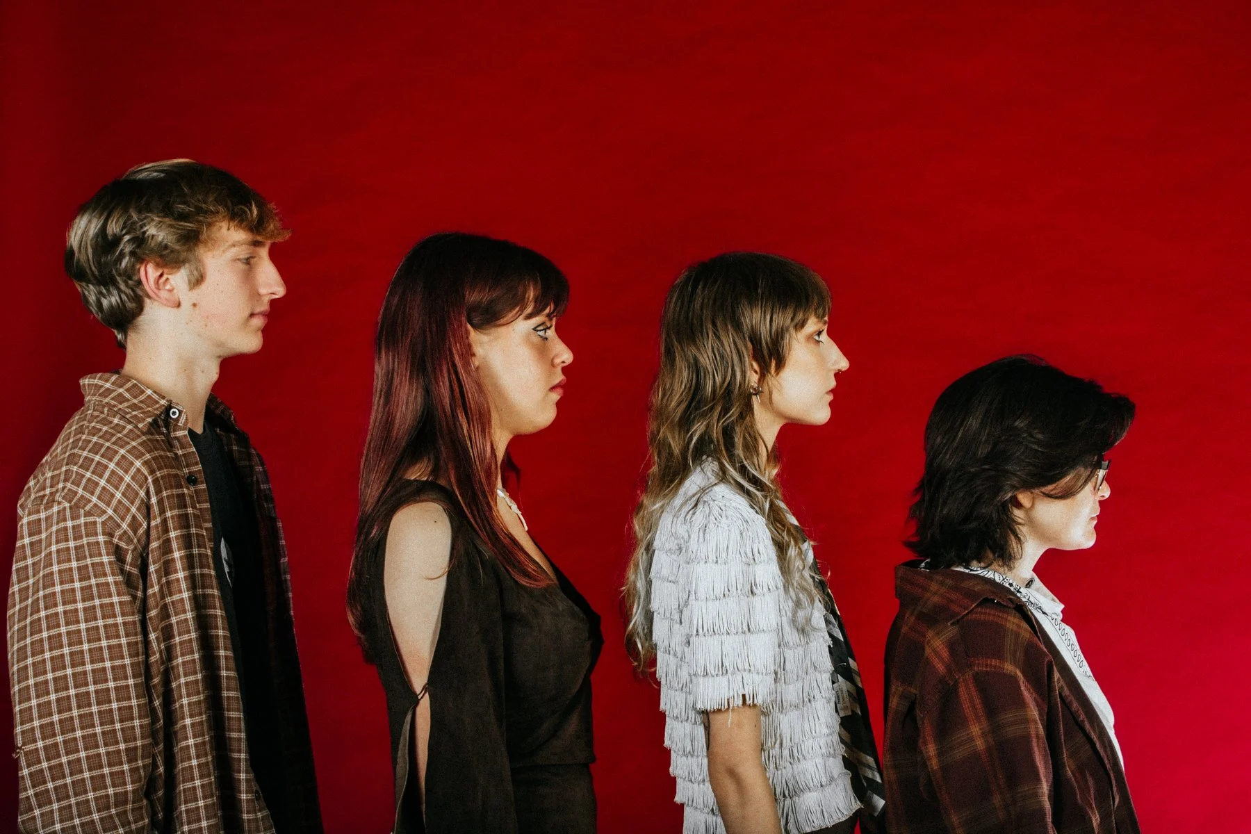 Five young women and men standing in profile against a red background, looking to the right, dressed in casual clothing.