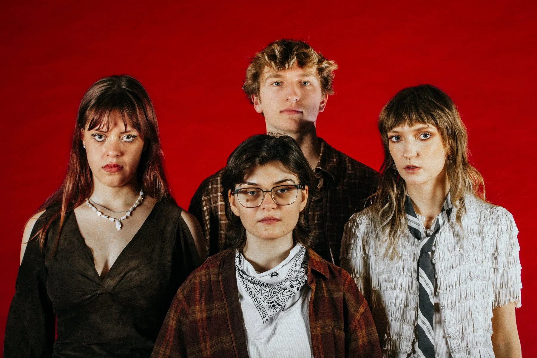 Group of five young adults standing against a red background, looking serious.