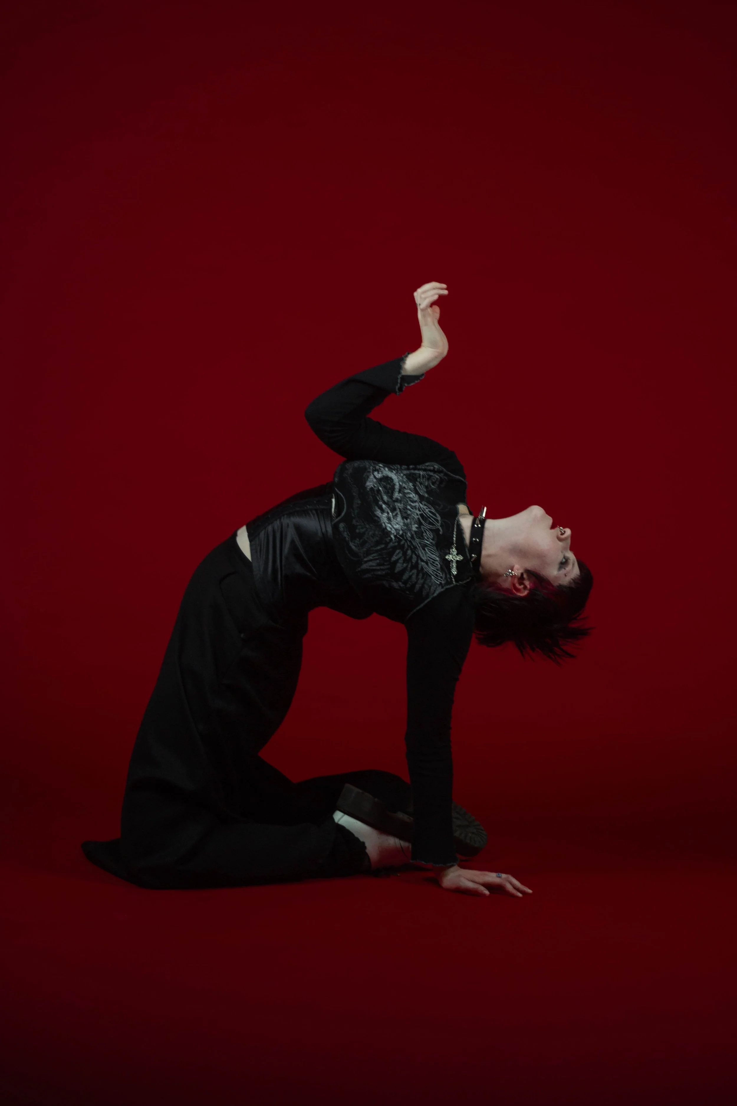 Person in black clothing and jewelry performing a yoga pose on a red background.