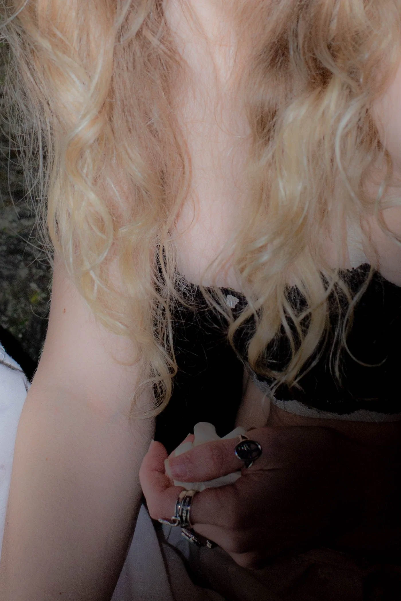 A close-up of a person with curly blonde hair and fair skin, wearing rings on their fingers and holding another person or object.