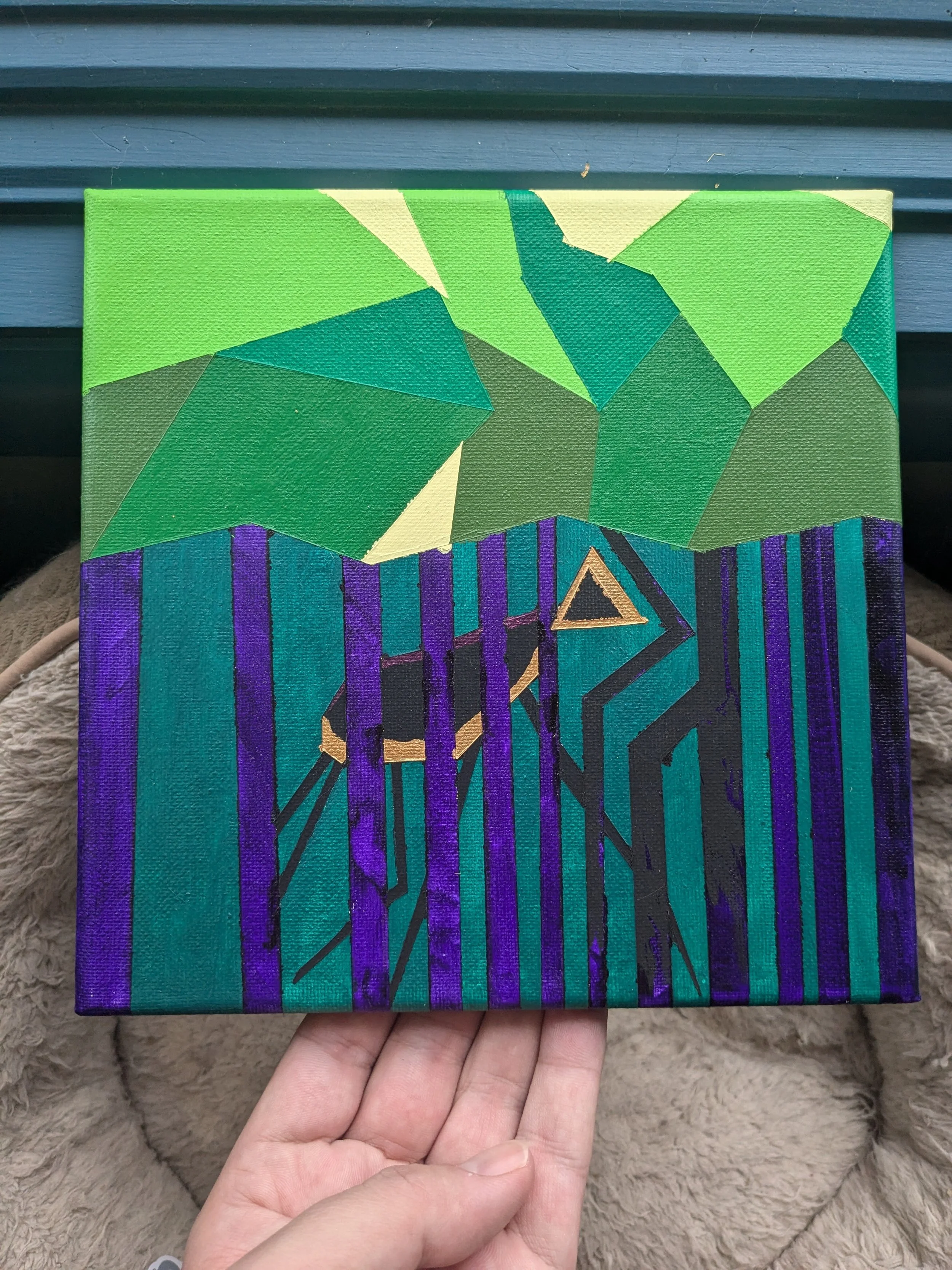 A person holding a rectangular painting with geometric shapes in varying shades of green, purple, and black, featuring a small gold triangle near the bottom.