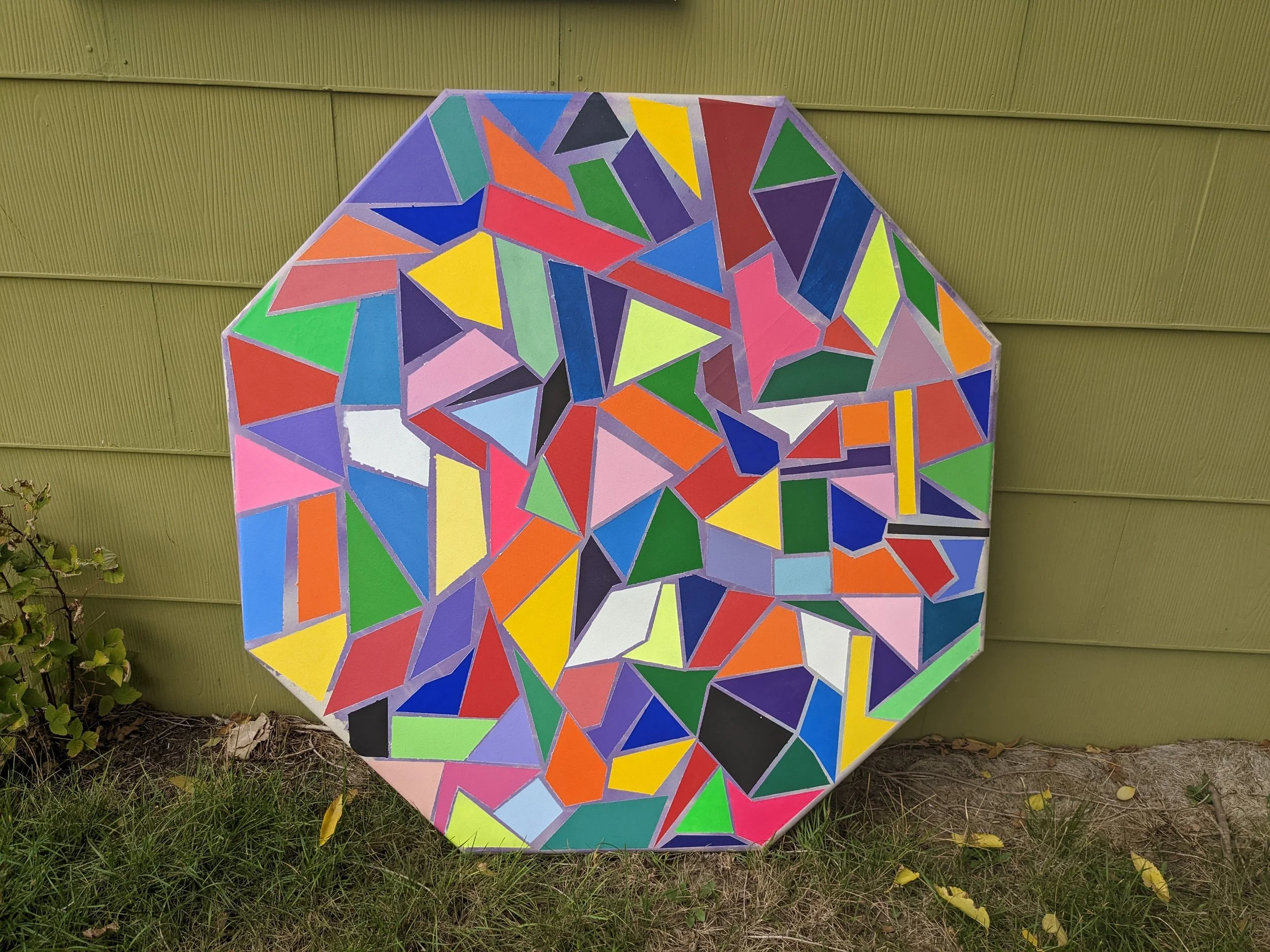 Colorful mosaic geometric pattern on a three-dimensional surface placed outdoors against a yellow wall.