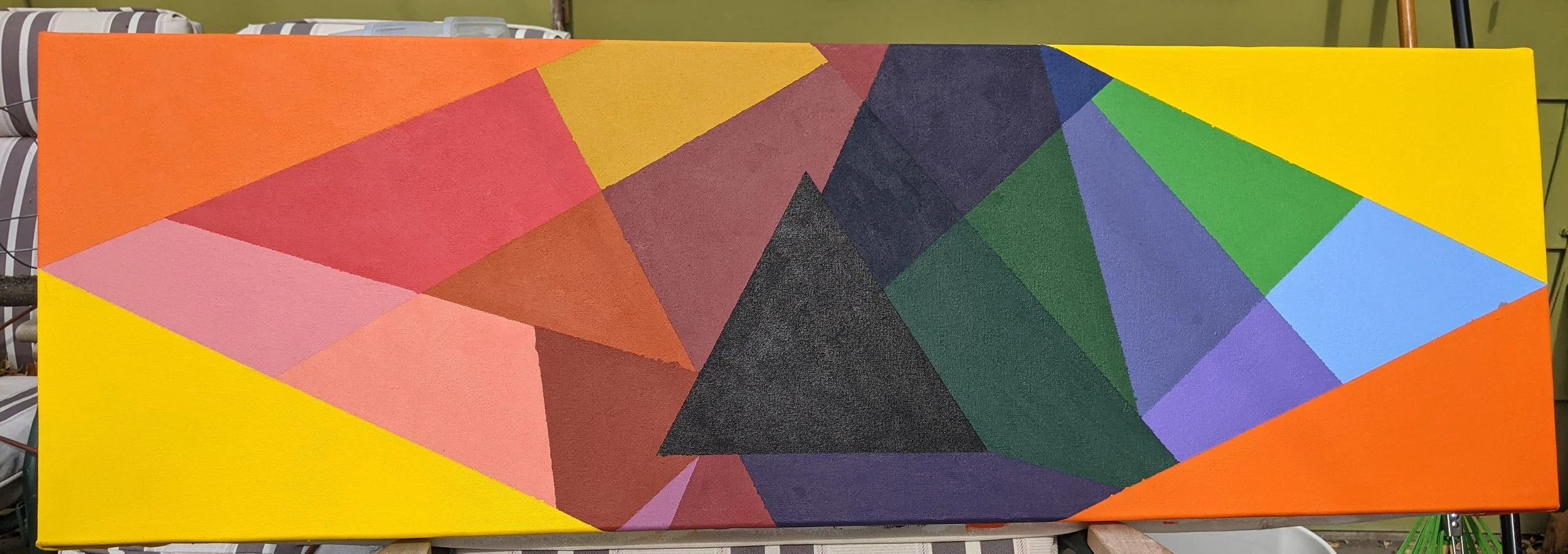A colorful abstract geometric painting with various shapes and shades, including yellow, orange, red, pink, purple, green, blue, and black, displayed on a rectangular canvas.