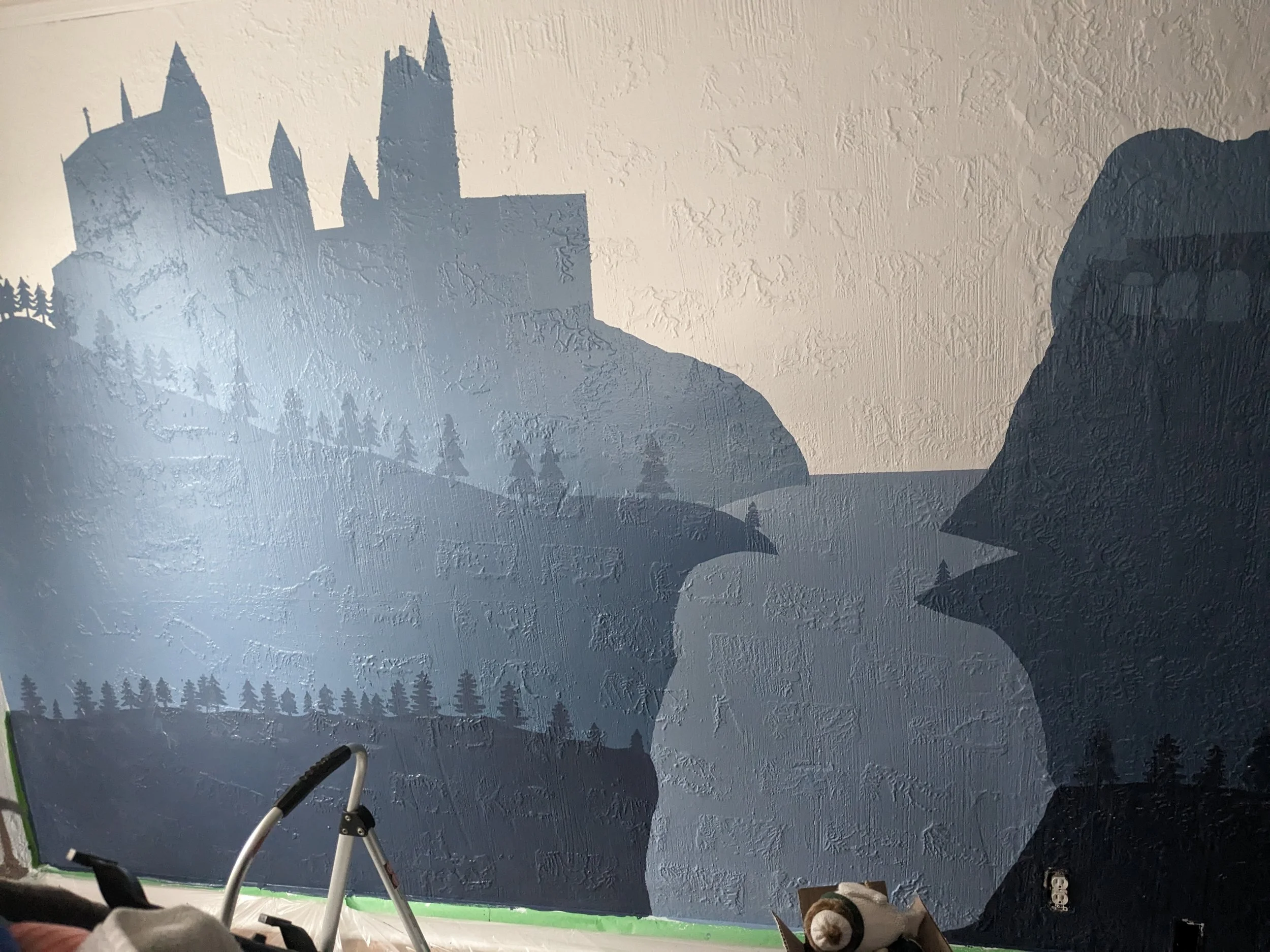 A large mural of a castle on a mountain with pine trees at the base, painted on a textured wall.