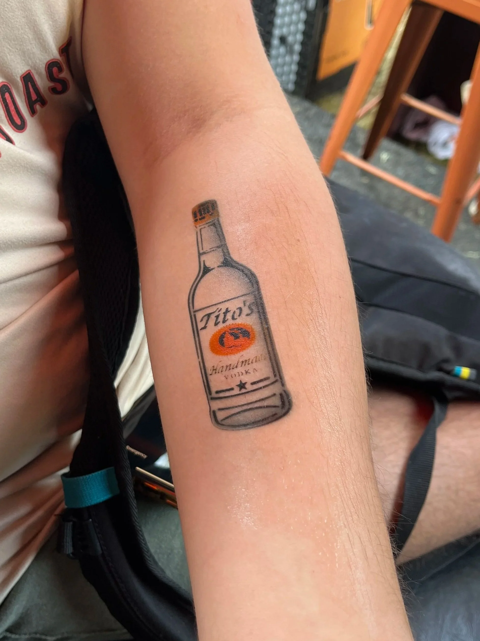 Temporary tattoo of a vodka bottle with the words "Tito's Handmade Vodka" on a person's forearm.