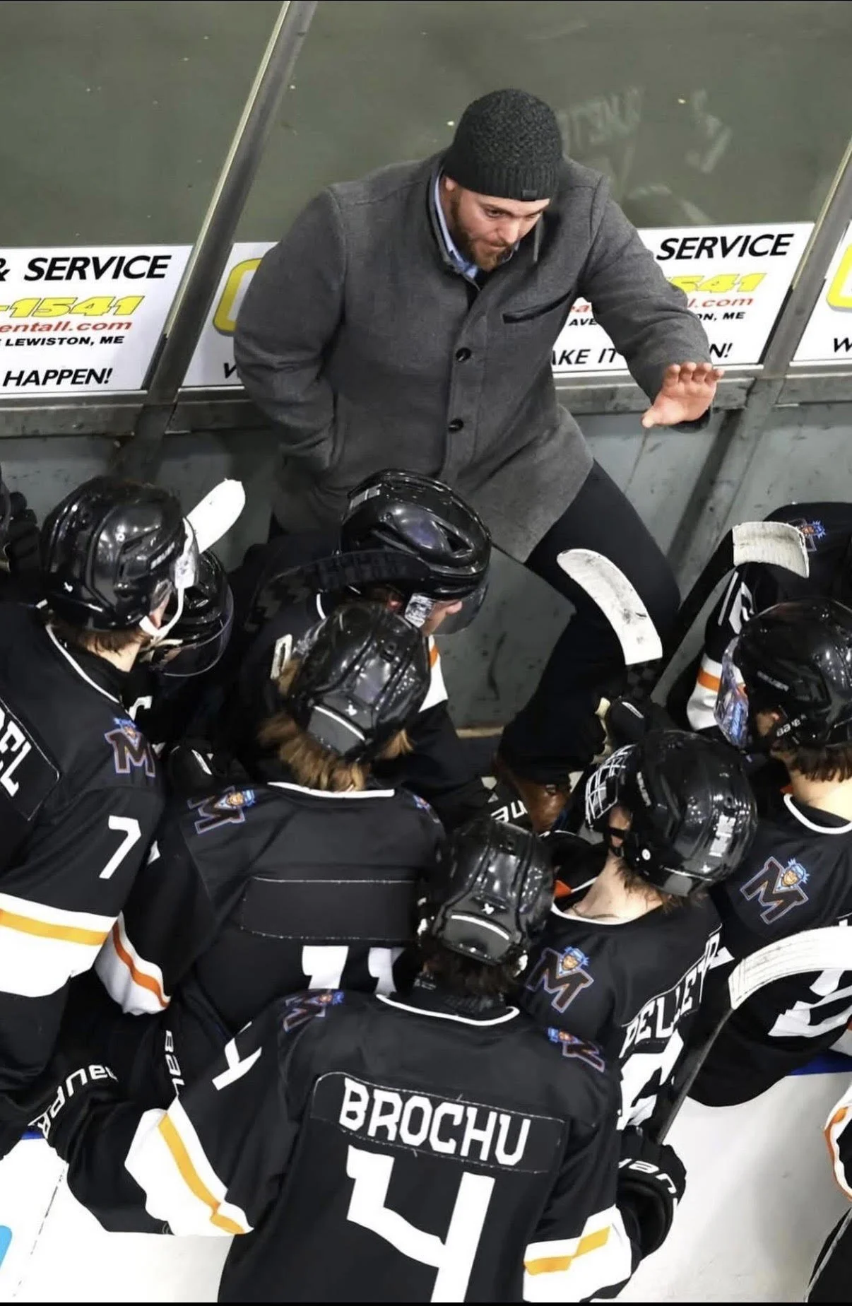 A hockey coach giving instructions to a team of young hockey players during a game or practice on the ice rink.