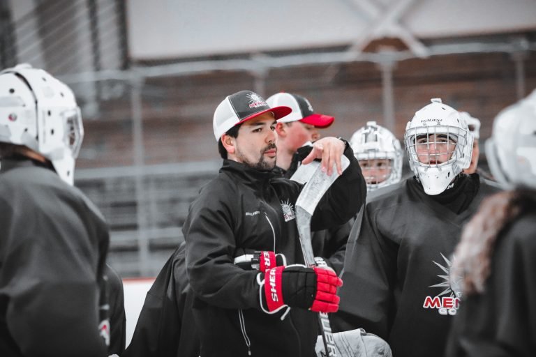 Hockey coach giving instructions to players during a team practice on the ice rink.