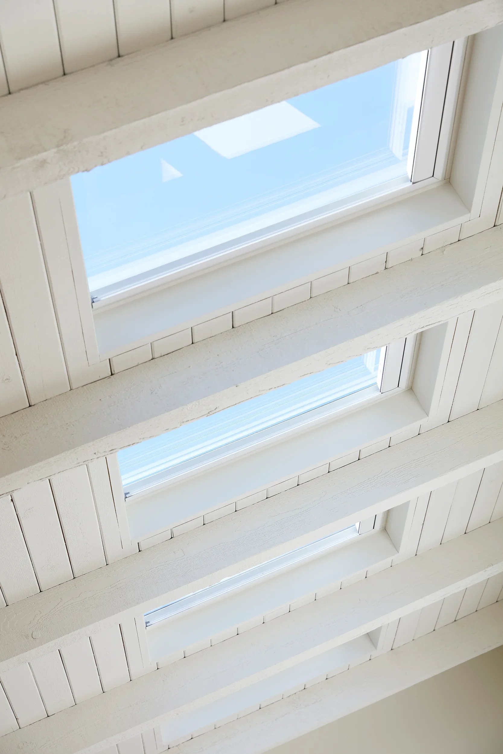 Looking up at a series of rectangular skylights in a white ceiling, with blue sky visible through the glass.